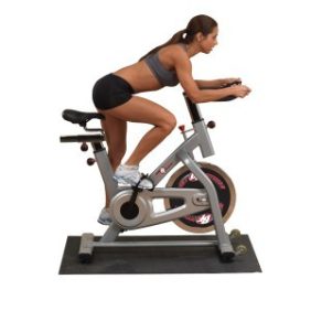 A woman riding a Body Solid Best Fitness Chain Indoor Bike - New on a white background while using new gym equipment.