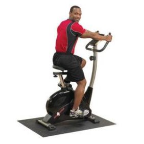 A man pedaling on a Body Solid Best Fitness Upright Bike - New placed on a fitness mat.