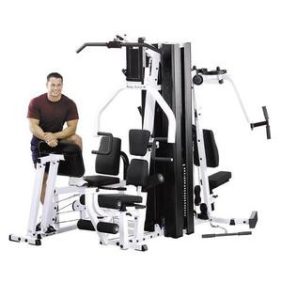 A man confidently posing in front of the Body-Solid EXM3000LPS Selectorized Home Gym System - New.