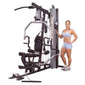A woman standing next to a Body Solid G5S Selectorized Home Gym - New.