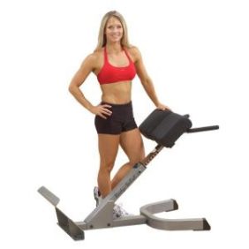 A woman is posing on a Body Solid Powerline 45 Degree Back Hyperextension - New machine at the gym.
