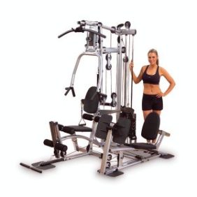A woman standing next to a Body Solid Powerline P2X Home Gym - New.
