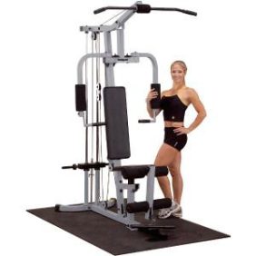 A woman standing next to a Body Solid Powerline PHG1000X Home Gym - New.