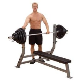 A man is standing on a Body Solid Pro Clubline Flat Olympic Bench - New, showcasing the use of new gym equipment.