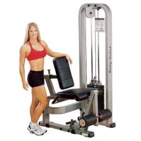 A woman is posing next to a new Body Solid Selectorized Pro Clubline Leg Extension Machine 210 lbs Stack - New.
