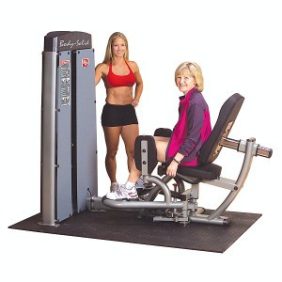 Two women standing next to a Body Solid Selectorized Pro Dual Inner Outer Thigh Machine - New.