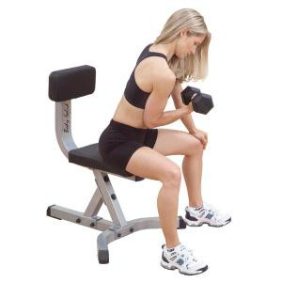 A woman is sitting on a bench with the Body Solid Utility Stool - New.