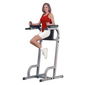 A woman is sitting on the Body Solid Vertical Knee Raise & Dip Station - New.