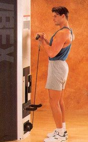 A man is standing in front of a Cybex Modular Standing Curl- Remanufactured machine.