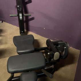 A Life Fitness Ab Crunch Bench - Remanufactured, featuring padded seats and backrest in black and gray, stands against a purple wall on a concrete floor.