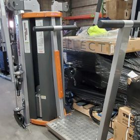 A Star Trac Human Sport Total Leg - As Is Functional machine sits amidst boxes and equipment in a storage area, blending seamlessly into the dynamic environment.