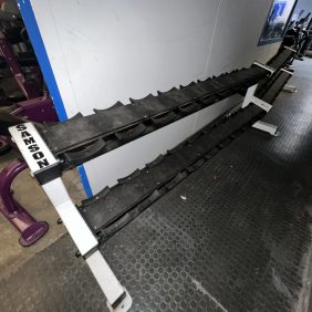 Two large serrated metal blades, likely from a Precor Stretch Machine - Remanufactured, are mounted on a white and purple frame placed on a dark textured floor.