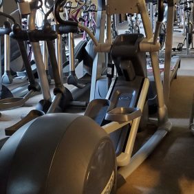 A row of serviced Precor AMT835 ellipticals lines the gym, their sleek design gleaming under the lights and mirrored walls, epitomizing premium fitness equipment.