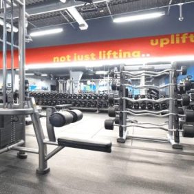 The "Package: As Is Functional" gym features bright lighting, multiple weight machines, and racks of dumbbells; a wall sign reads, "not just lifting... uplifting.