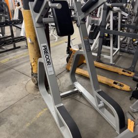The Revolution Fitness exercise machine, ideal for core workouts with its padded backrest and grips, stands alongside the Matrix Leg Press - As Is Functional on a sturdy concrete floor setup, perfect for fitness enthusiasts.