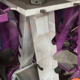 The Cable Attachment Accessory Rack - As Is Functional is shown in purple and white metal, with orange buckets and rolled-up mats placed on the floor in front.