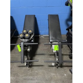 Two black Flat - 90 Degree - Remanufactured adjustable weight benches, each with a sturdy metal frame and leg rollers, are positioned flat against a blue wall on a concrete floor.