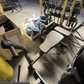 A Life Fitness Ab Bench - As Is Functional is stored in a storage area with other gym equipment and assorted items, including a nearby box containing fabric and parts.